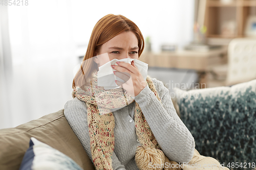 Image of sick woman blowing nose in paper tissue at home
