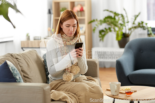 Image of sad sick woman in scarf with smartphone at home