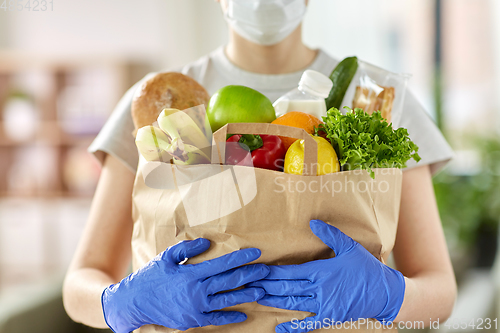 Image of woman in gloves with food in paper bag at home