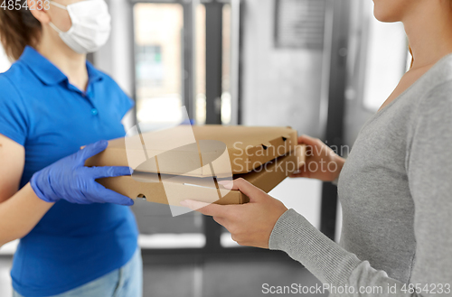 Image of delivery girl in mask giving pizza boxes to woman