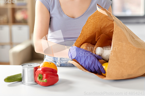 Image of woman in gloves taking food from paper bag at home