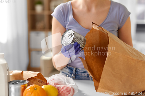 Image of woman in gloves taking food from paper bag at home