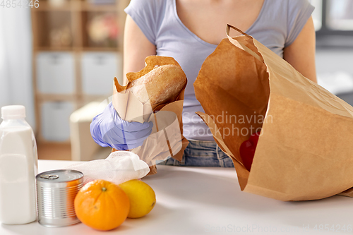 Image of woman in gloves taking food from paper bag at home
