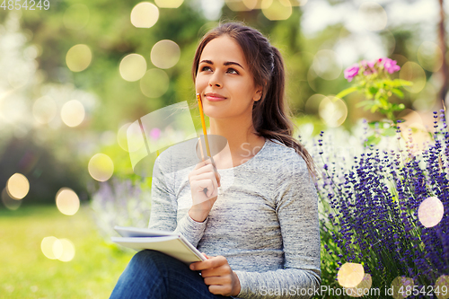 Image of young woman writing to notebook at summer garden