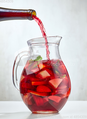 Image of red wine pouring into jug of cutted fruits