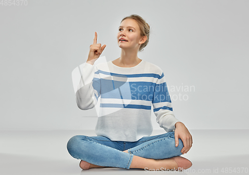 Image of teenage girl pointing finger up sitting on floor