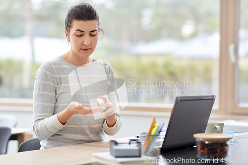 Image of woman spraying hand sanitizer at home office