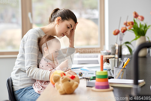 Image of tired mother with baby working at home office