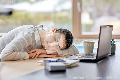 Image of tired woman sleeping on table with laptop at home