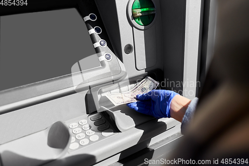 Image of hand in medical glove with money at atm machine