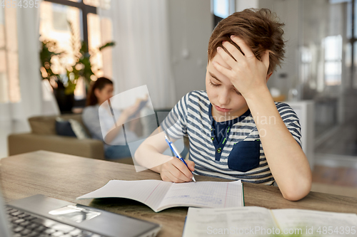 Image of student boy with book writing to notebook at home