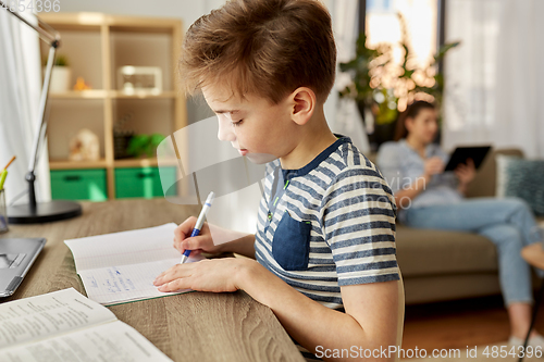 Image of student boy with book writing to notebook at home