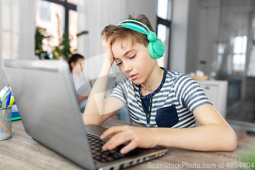 Image of sad boy with laptop and headphones at home