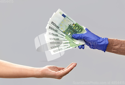 Image of one hand in medical glove giving money to another