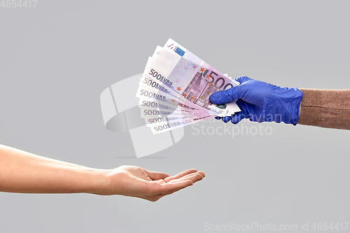 Image of one hand in medical glove giving money to another