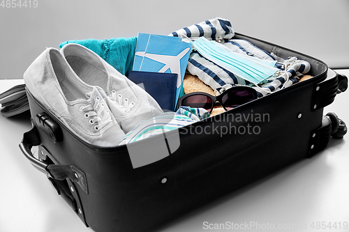 Image of travel bag packed with clothes, tickets and masks