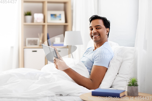 Image of happy indian man with tablet pc in bed at home