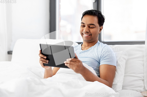 Image of happy indian man with tablet pc in bed at home