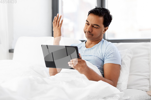 Image of indian man with tablet pc in bed at home