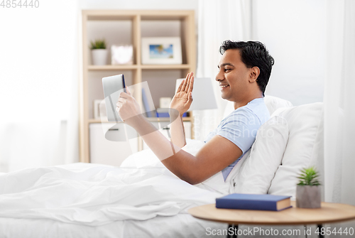 Image of happy man with tablet pc in bed having video call