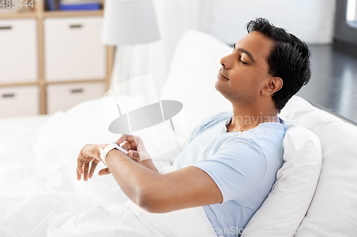 Image of happy indian man with smart watch in bed at home