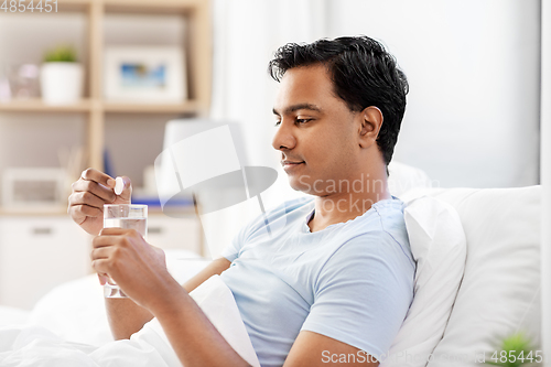 Image of man in bed dropping medicine into glass of water