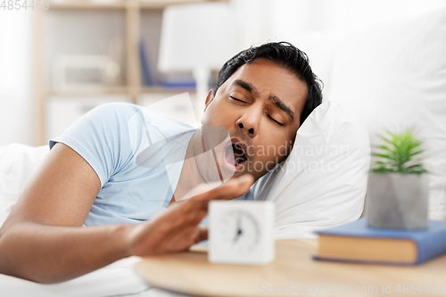 Image of sleepy indian man with alarm clock in bed yawing