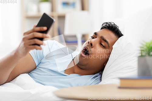 Image of sleepy indian man with smartphone lying in bed