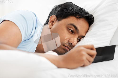 Image of sleepy indian man with smartphone lying in bed