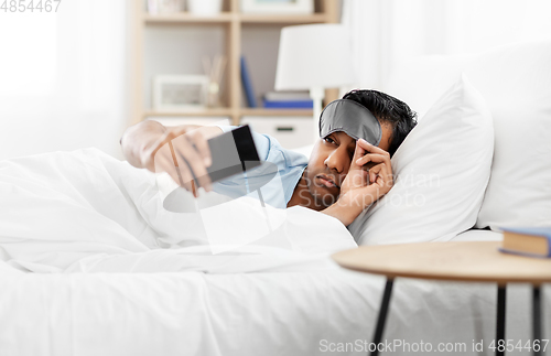 Image of sleepy indian man with smartphone lying in bed