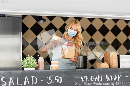 Image of saleswoman in mask making wok at food truck