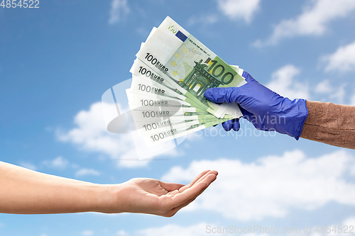 Image of one hand in medical glove giving money to another