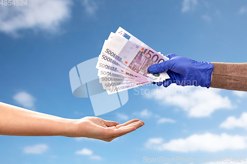 Image of one hand in medical glove giving money to another