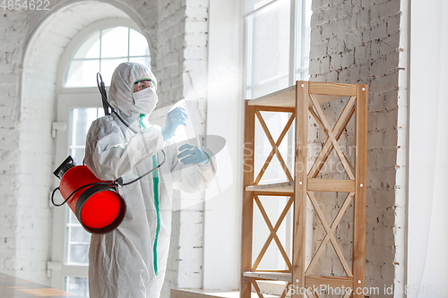 Image of Coronavirus Pandemic. A disinfector in a protective suit and mask sprays disinfectants in the house or office