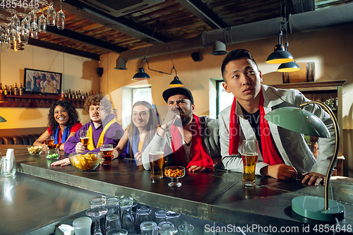 Image of Sport fans cheering at bar, pub and drinking beer while championship, competition is going