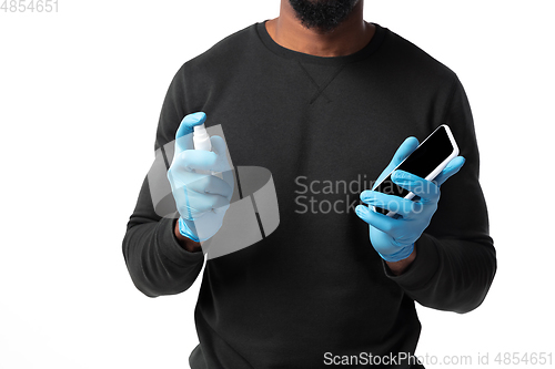 Image of How coronavirus changed our lives. Young man disinfecting gadgets surfaces on white background