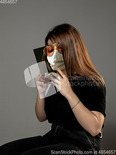 Image of Be safe and read to become someone else - woman covering face with book in face mask while reading on grey background