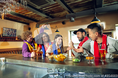 Image of Sport fans cheering at bar, pub and drinking beer while championship, competition is going