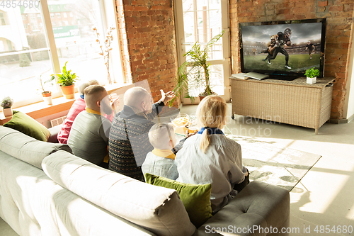 Image of Excited family watching american football, sport match at home