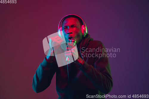 Image of African-american man\'s portrait with headphones isolated on gradient studio background in neon light