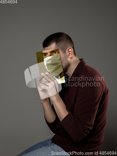 Image of Be safe and read to become someone else - man covering face with book in face mask while reading on grey background