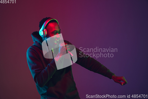 Image of African-american man\'s portrait with headphones isolated on gradient studio background in neon light