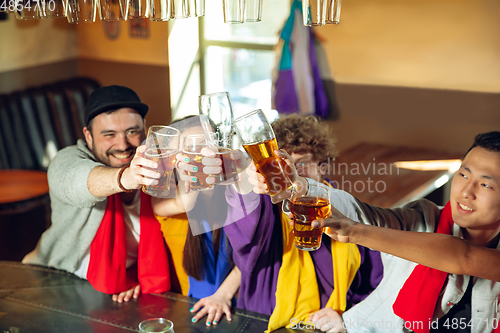 Image of Sport fans cheering at bar, pub and drinking beer while championship, competition is going