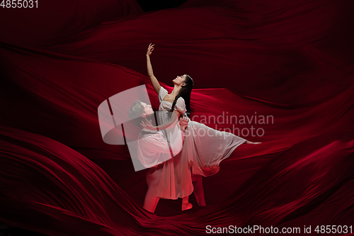 Image of Young and graceful ballet dancers on billowing red cloth background in classic action. Art, motion, action, flexibility, inspiration concept.