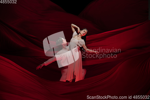 Image of Young and graceful ballet dancers on billowing red cloth background in classic action. Art, motion, action, flexibility, inspiration concept.