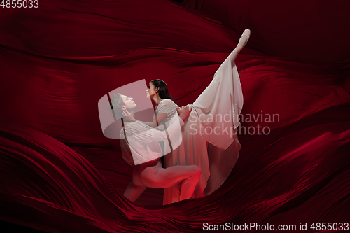 Image of Young and graceful ballet dancers on billowing red cloth background in classic action. Art, motion, action, flexibility, inspiration concept.