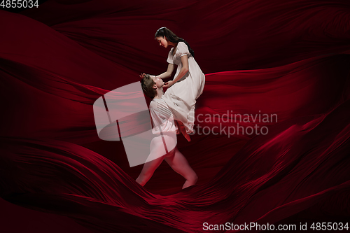 Image of Young and graceful ballet dancers on billowing red cloth background in classic action. Art, motion, action, flexibility, inspiration concept.