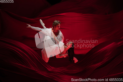 Image of Young and graceful ballet dancers on billowing red cloth background in classic action. Art, motion, action, flexibility, inspiration concept.