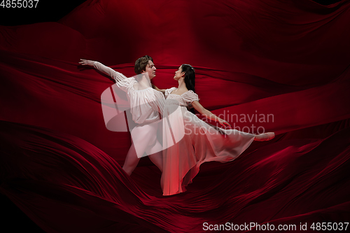 Image of Young and graceful ballet dancers on billowing red cloth background in classic action. Art, motion, action, flexibility, inspiration concept.