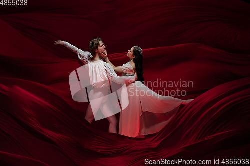 Image of Young and graceful ballet dancers on billowing red cloth background in classic action. Art, motion, action, flexibility, inspiration concept.